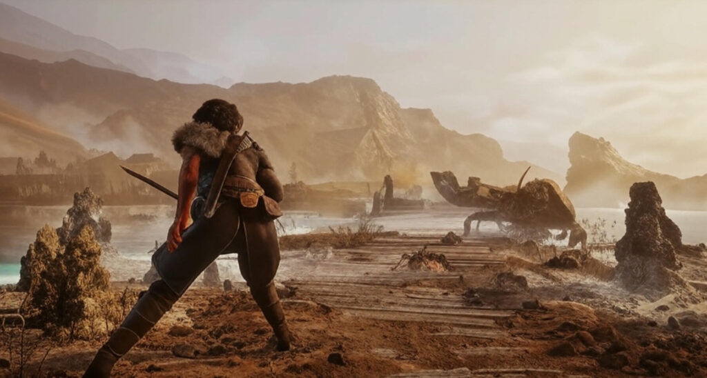 A warrior in rugged armor and fur-lined clothing stands on a wooden path in a desolate, misty landscape, wielding a sword and facing a large, menacing creature with claws and a segmented body. The scene features rocky terrain, scattered ruins, a calm body of water, and rugged mountains under a hazy, golden sky.